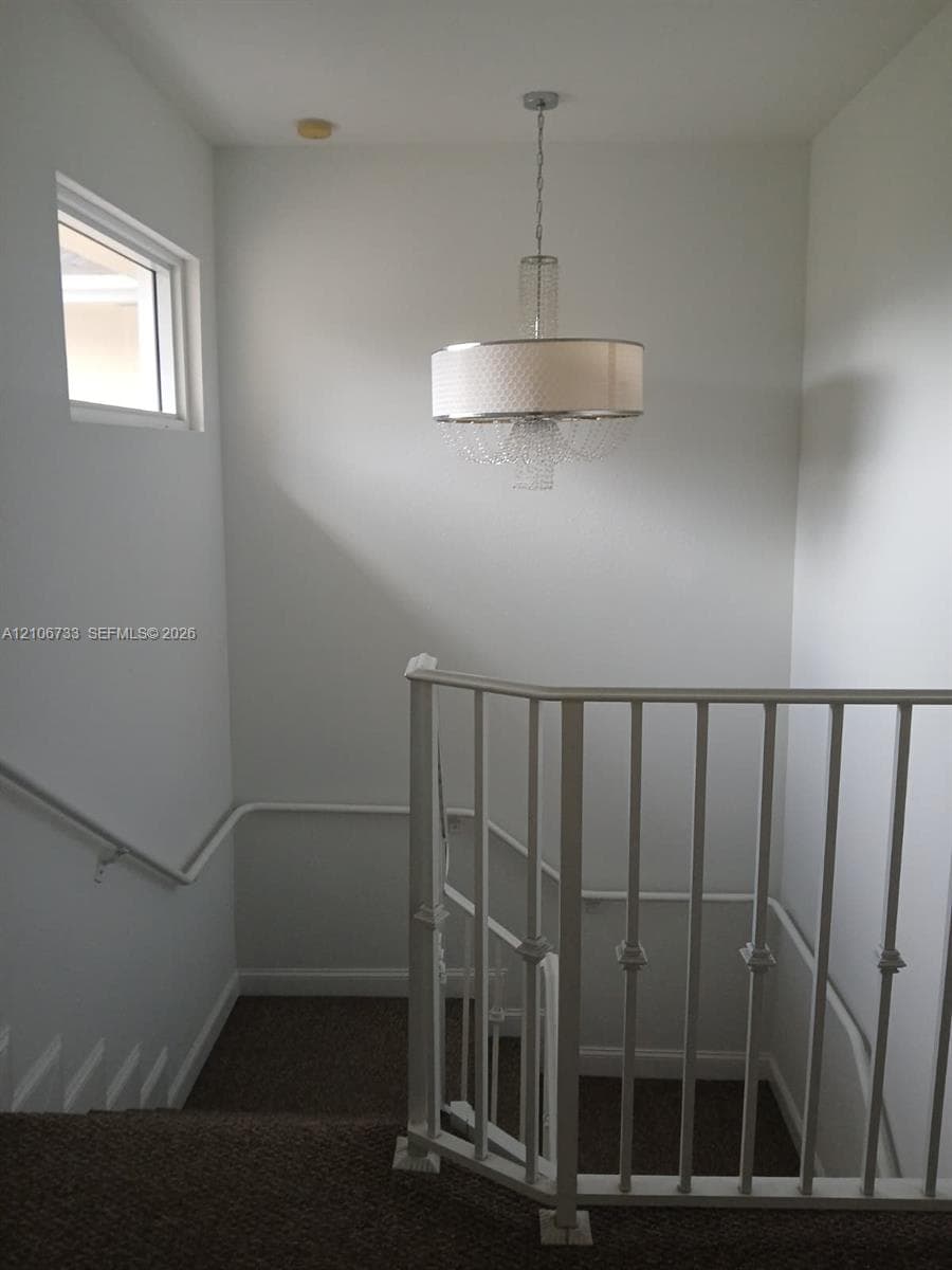 Drum-style pendant chandelier with crystal accents, white metal railing, and high-reaching ceiling