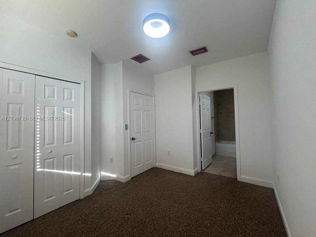 Room featuring wall-to-wall carpeting, dual-panel closet doors, single-panel interior doors, and a ceiling-mounted flush-mount light fixture