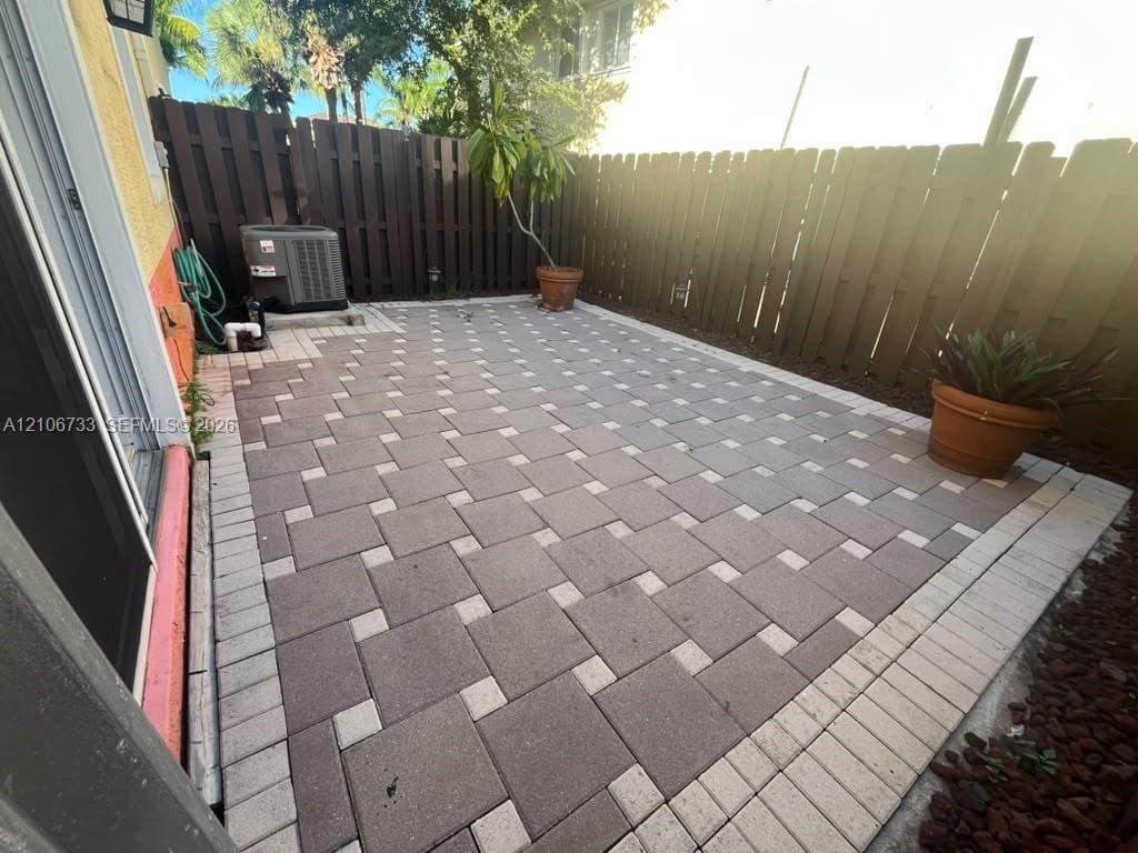 Private outdoor patio featuring interlocking concrete pavers, a decorative border, and a perimeter privacy fence