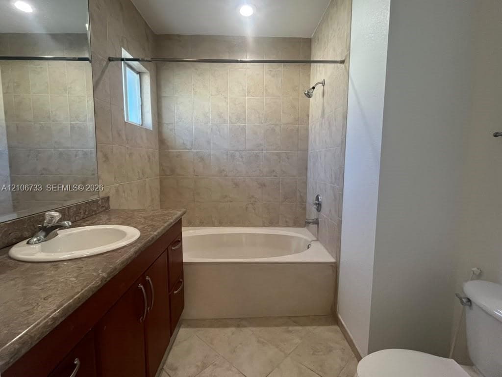 Bathroom featuring a wood-finish vanity with a stone-composite countertop, integrated sink, porcelain tile flooring, and a tiled shower surround with a soaking tub