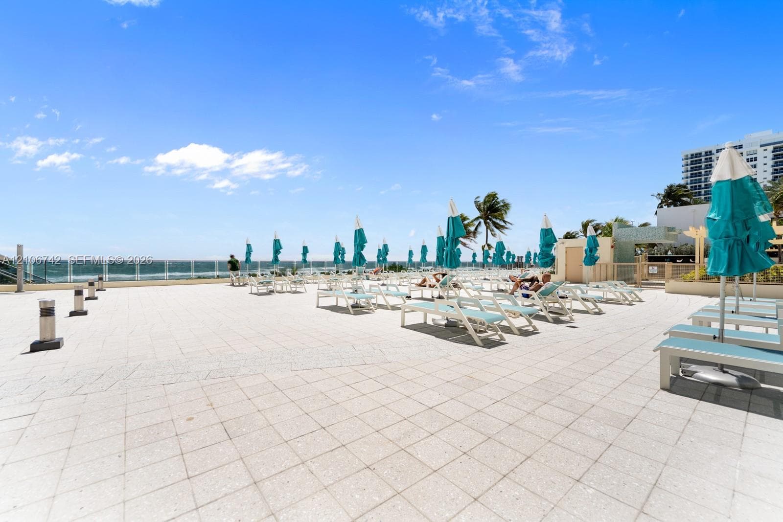 Expansive paved terrace featuring a glass panel railing, ocean backdrop, and integrated low-profile lighting fixtures