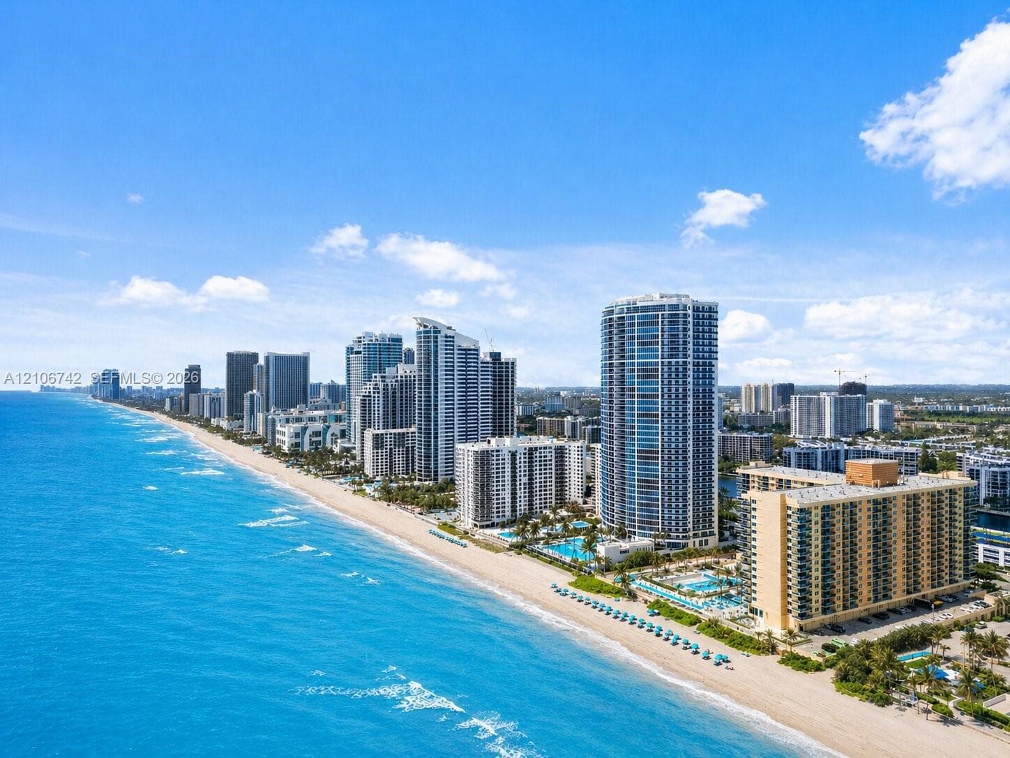 Aerial perspective of coastal high-rise development featuring direct beach access, expansive shoreline, and multi-story architectural structures