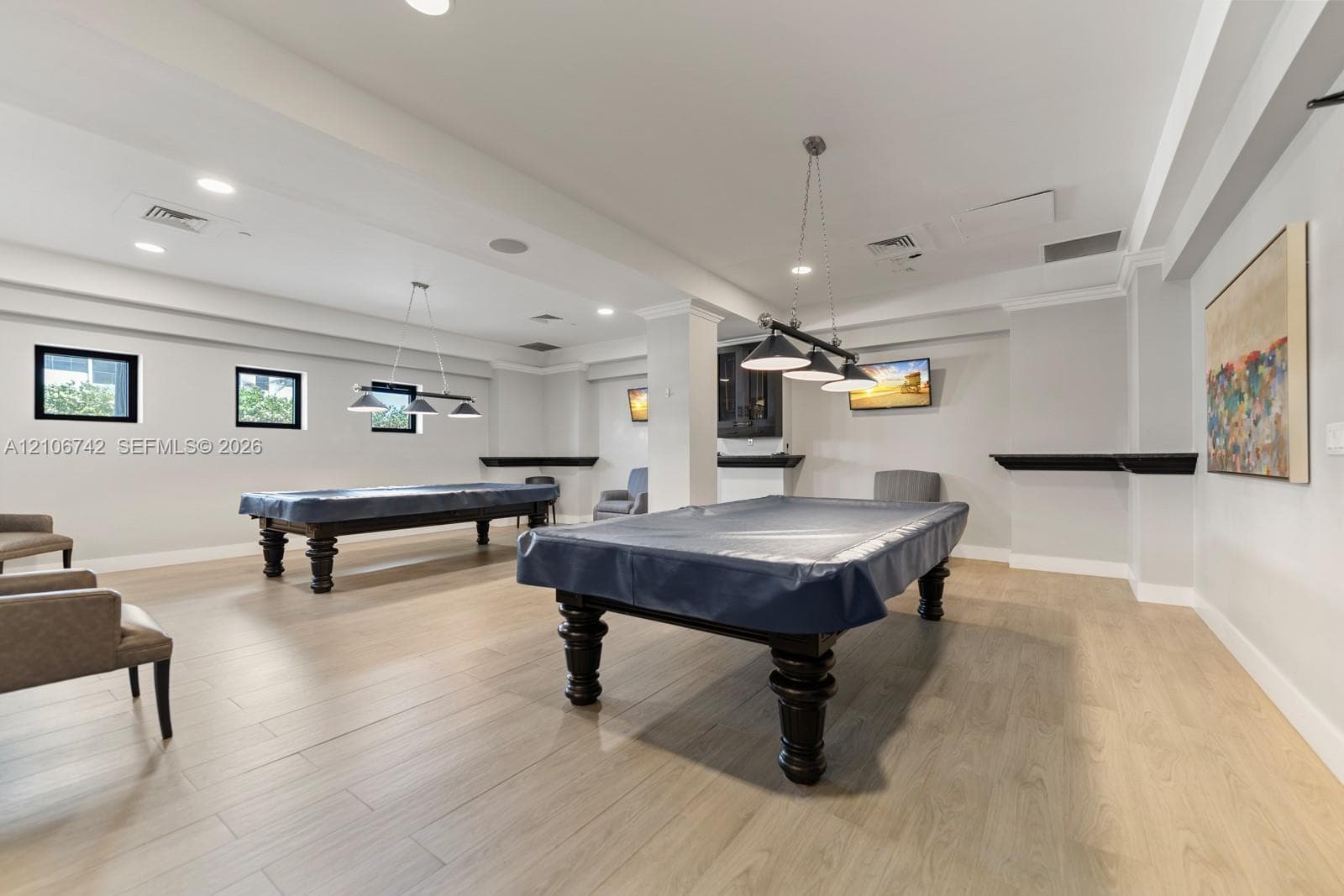 Spacious interior featuring wood-finish flooring, recessed lighting, crown molding, multi-light pendant fixtures, and built-in shelving ledges