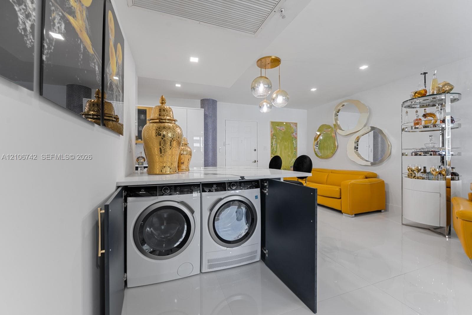 Built-in laundry area featuring high-gloss cabinetry, stone-surface countertop, recessed lighting, and sleek tile flooring
