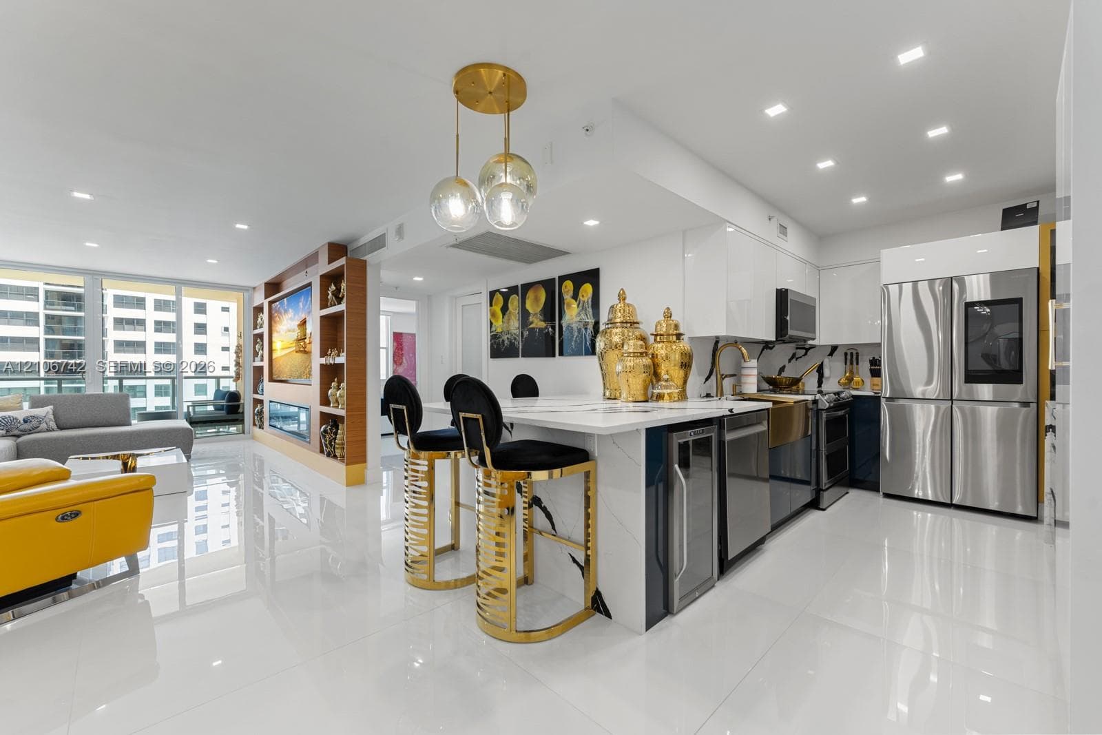 Open-concept kitchen featuring high-gloss cabinetry, a central waterfall-edge island, stainless steel appliances, and integrated beverage refrigeration