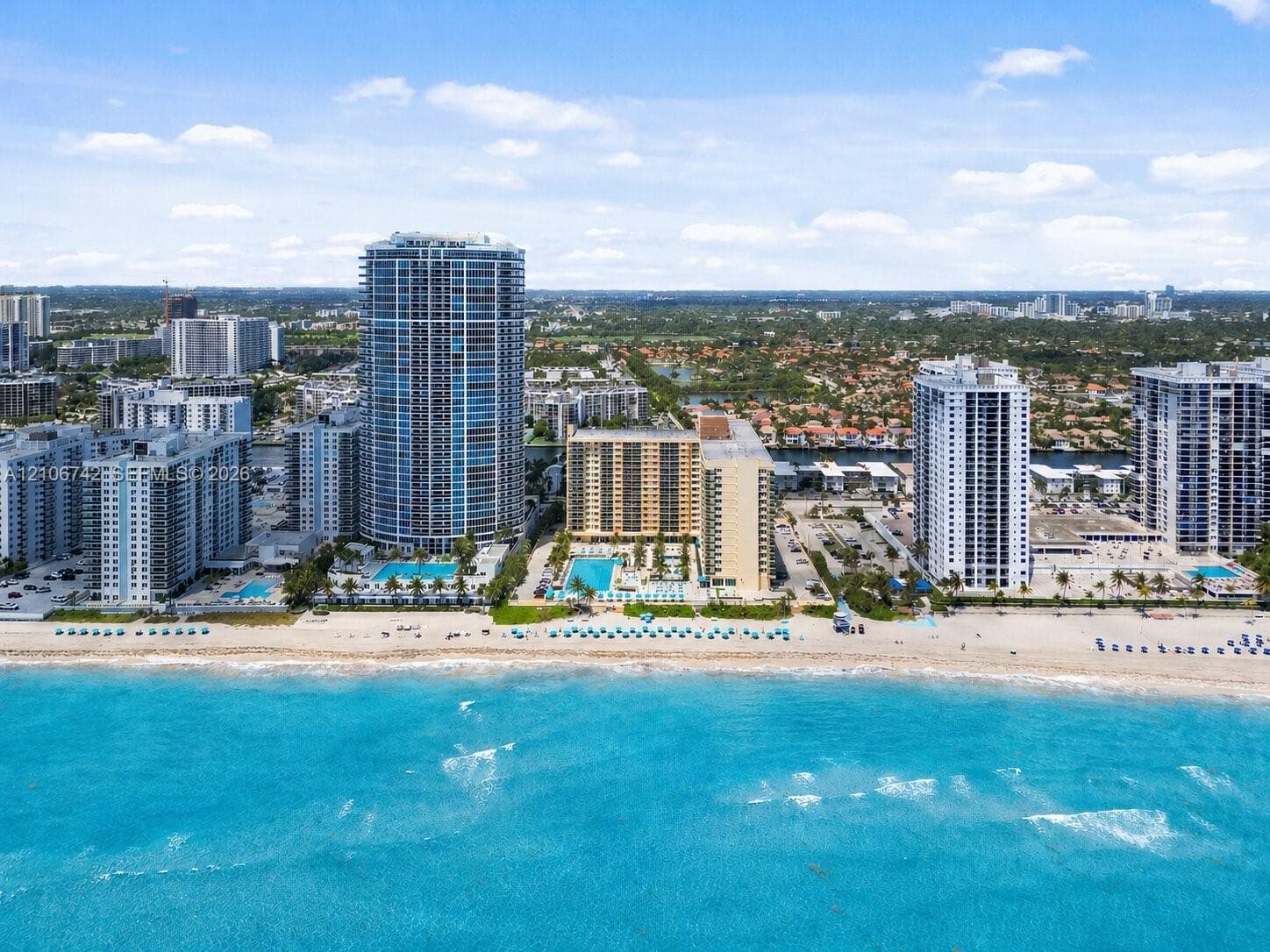 High-rise coastal property featuring direct oceanfront access, private swimming pool, landscaped grounds, and paved parking areas