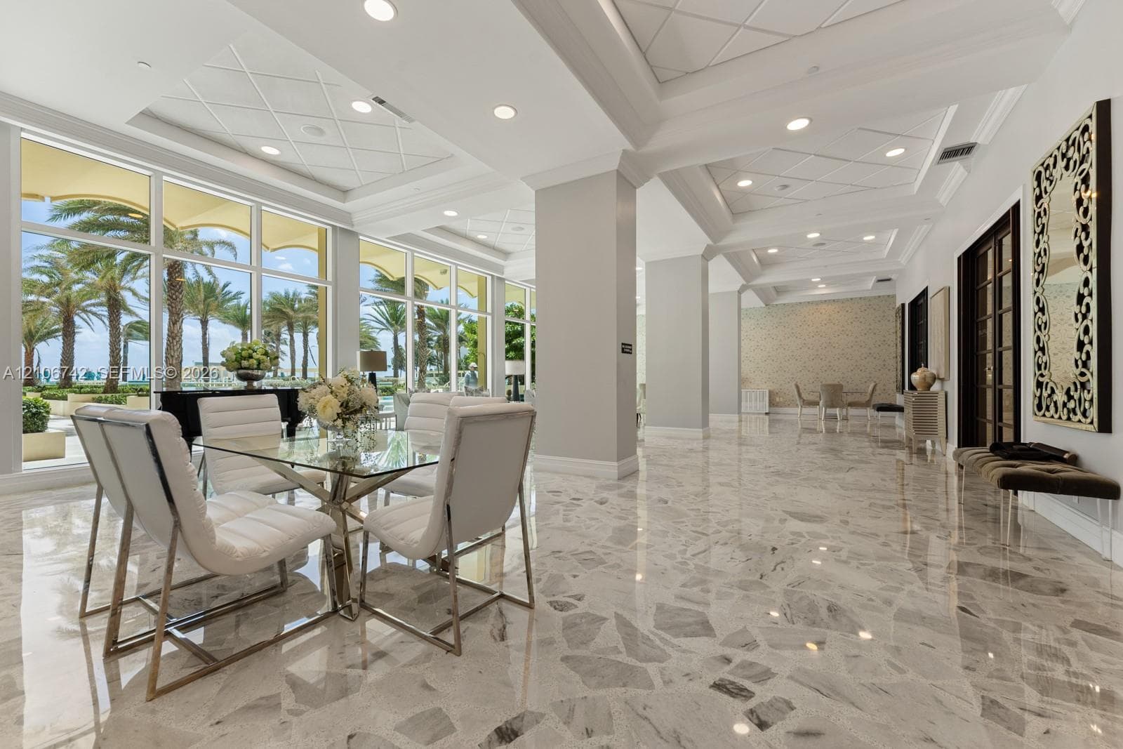 Expansive space featuring polished stone flooring, intricate coffered tray ceilings with recessed lighting, and floor-to-ceiling windows