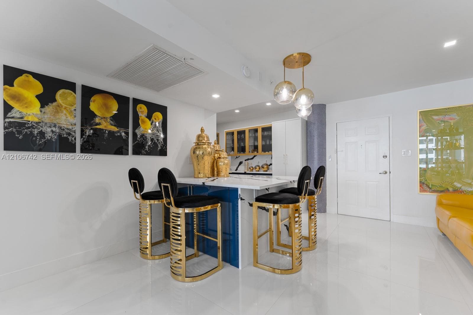 Kitchen island featuring a waterfall-edge stone countertop, deep blue base cabinetry, integrated pendant lighting, and polished gold-tone hardware