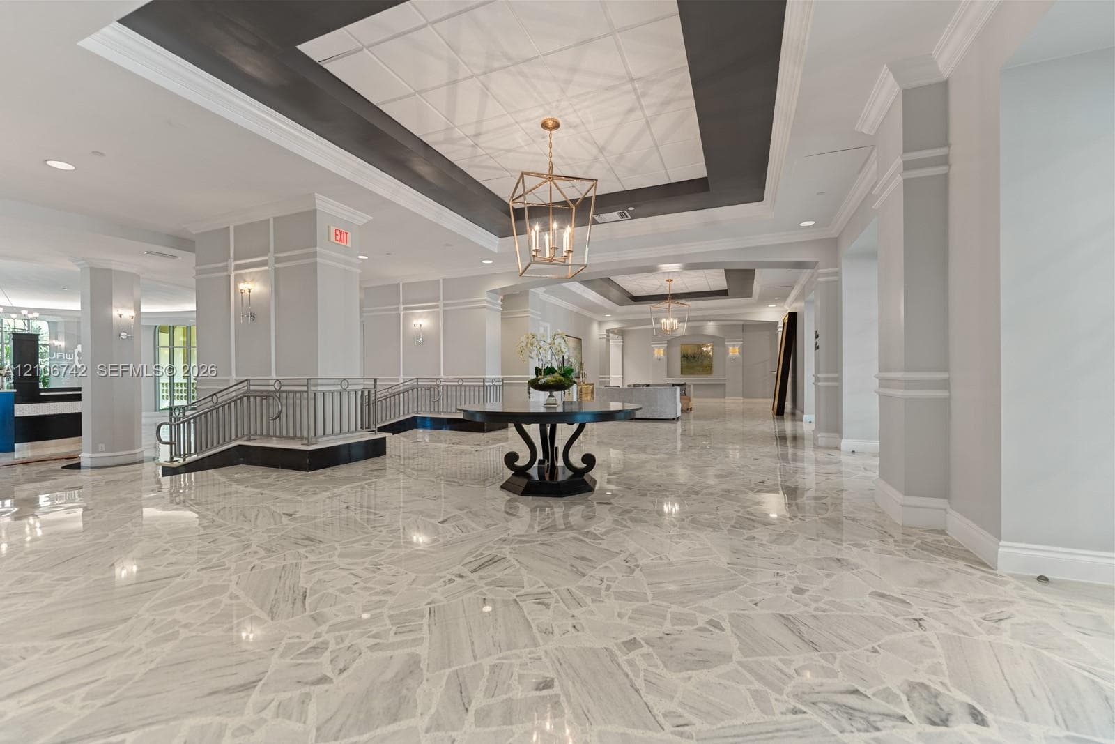Grand foyer featuring polished stone flooring, recessed coffered ceilings, decorative wainscoting, architectural columns, and geometric metal pendant lighting