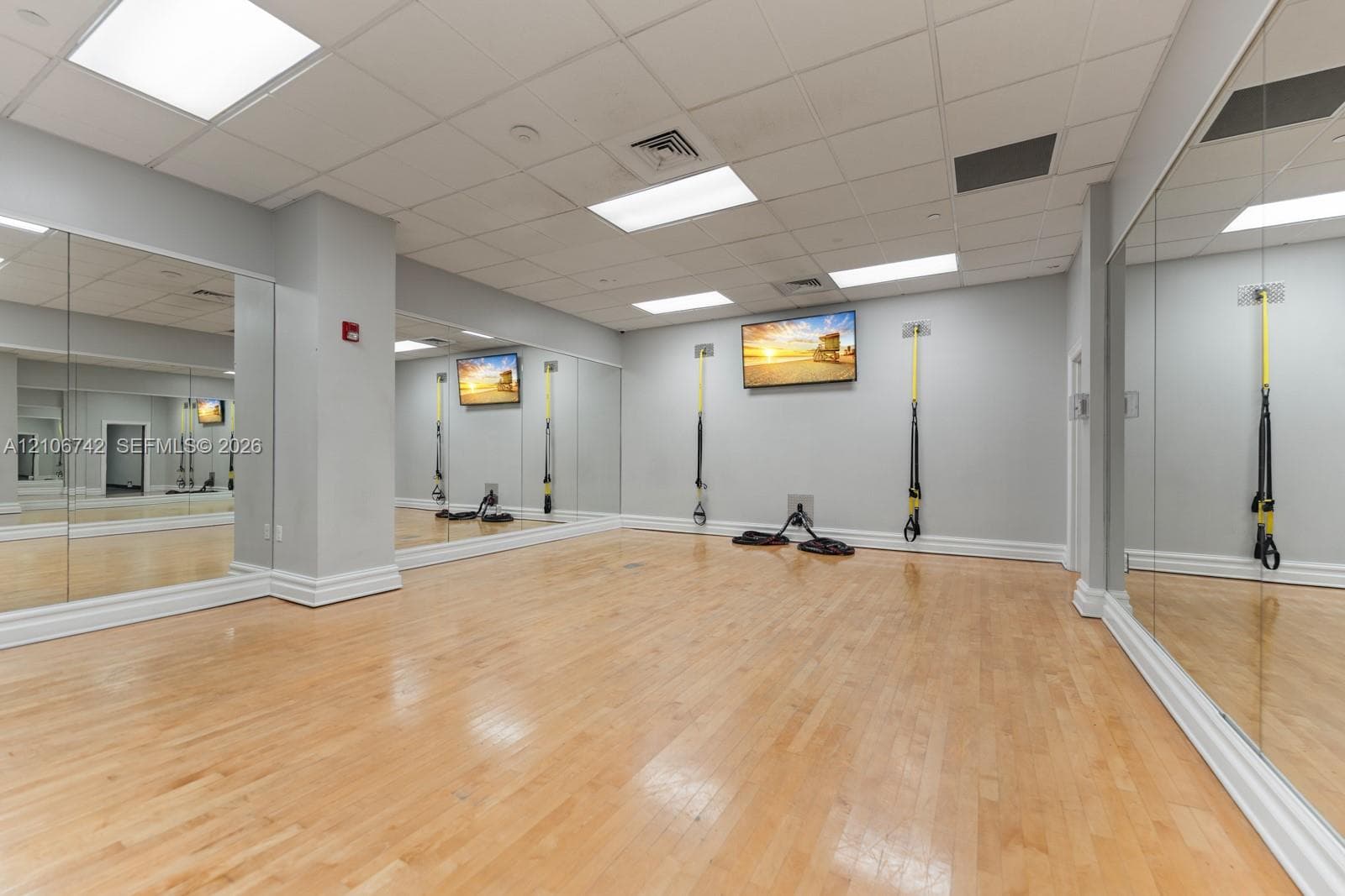 Dedicated fitness space featuring wood-finish flooring, full-length wall mirrors, recessed ceiling lighting, and wall-mounted suspension training equipment
