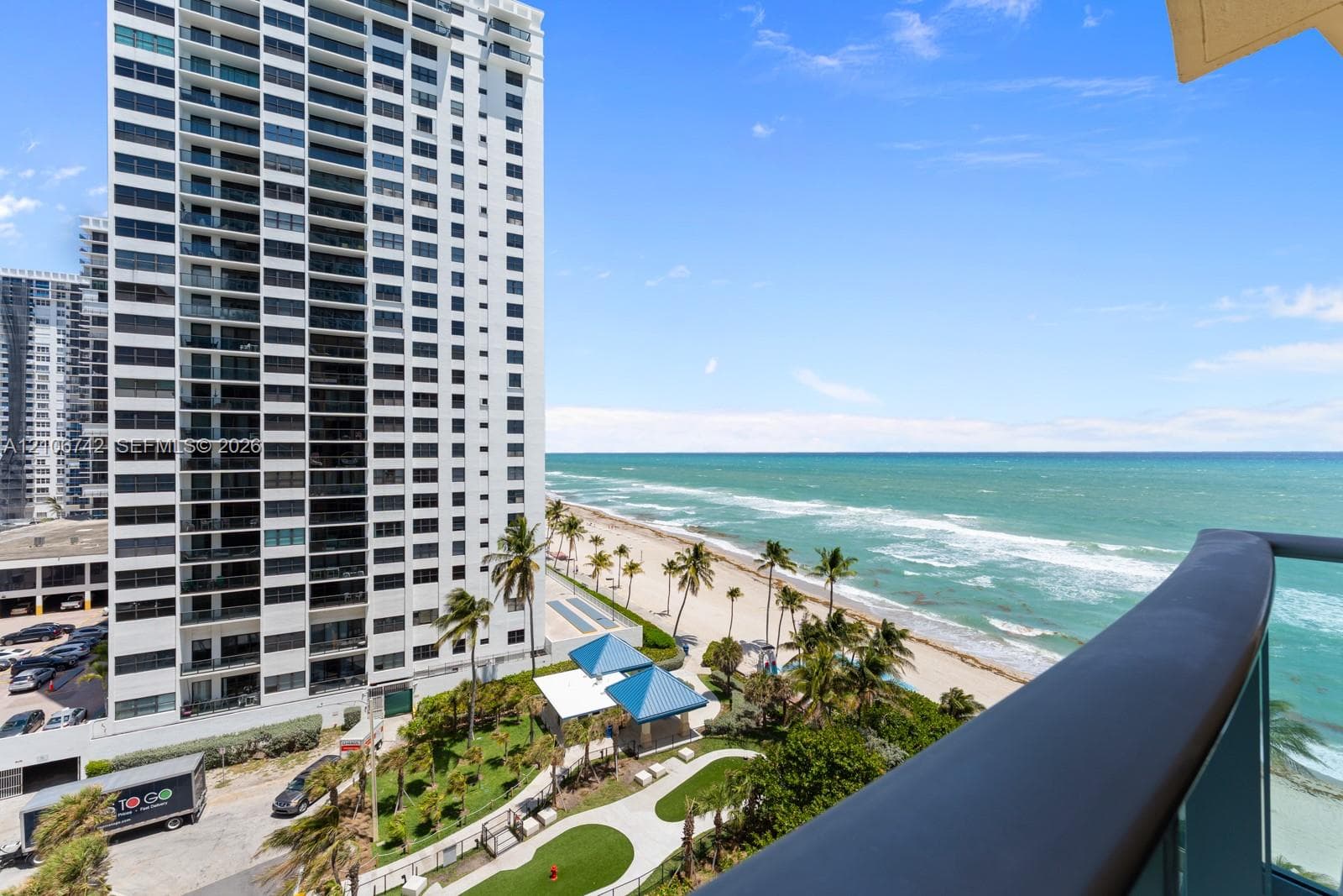 Balcony featuring a glass panel railing, panoramic oceanfront scenery, sandy beach access, and mature palm trees