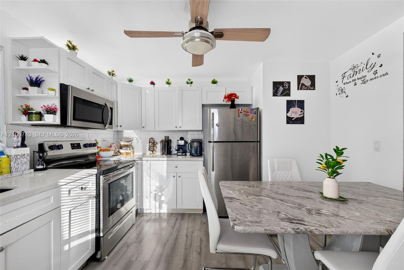 Kitchen featuring white Shaker-style cabinetry, stainless steel appliances, light-toned stone-patterned countertops, wood-finish flooring, and a ceiling-mounted light and fan fixture