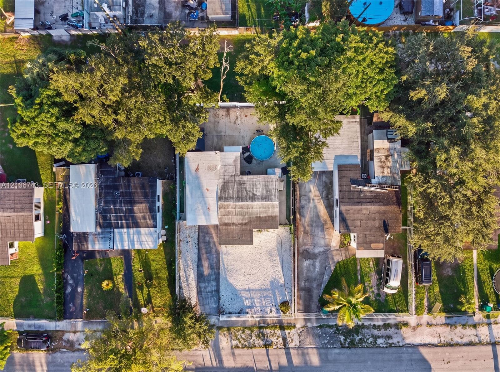 Aerial perspective of a residential property featuring a paved driveway, a backyard area with mature trees, and a circular above-ground pool