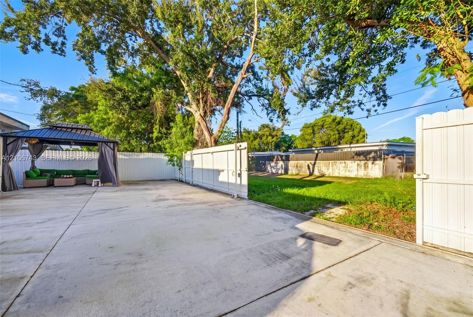 Backyard featuring a concrete patio, white vinyl fencing, grass lawn, and mature trees