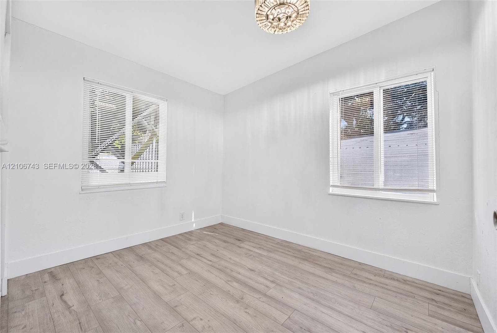 Interior room featuring wood-finish flooring, two windows with horizontal blinds, and a drum-style ceiling light fixture