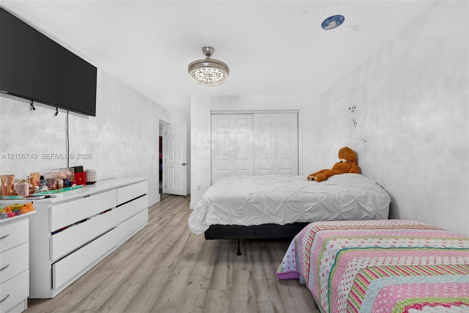 Wood-finish flooring, sliding closet doors with six-panel detailing, and a multi-light flush-mount ceiling fixture