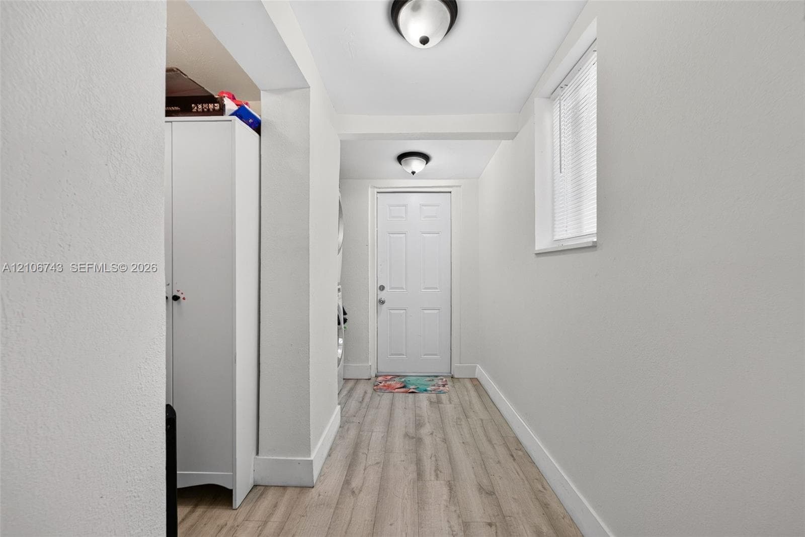 Entryway featuring wood-finish flooring, two dome-style flush-mount ceiling light fixtures, a white multi-panel door, and a horizontal window with blinds