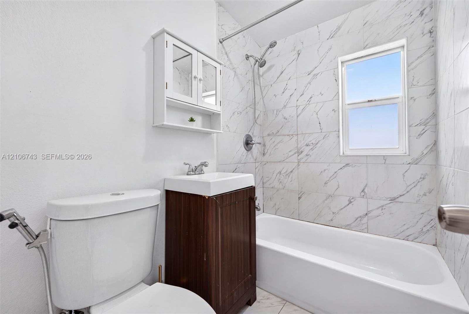 Bathroom featuring a tub and shower combination with full-height stone-finish wall tile, a wood-finish vanity with an integrated sink, and a wall-mounted medicine cabinet