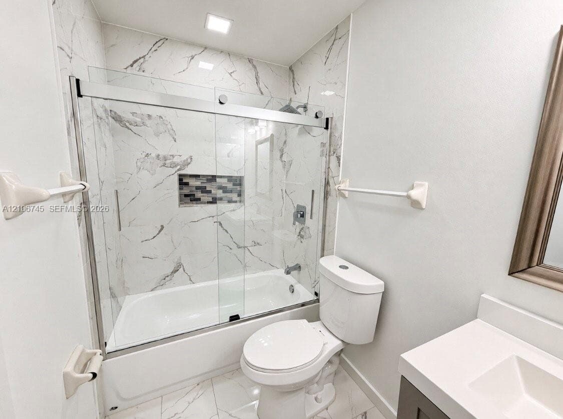 Full-height shower surround with veined tile, sliding glass shower door, integrated wall niche, and vanity with stone-style countertop