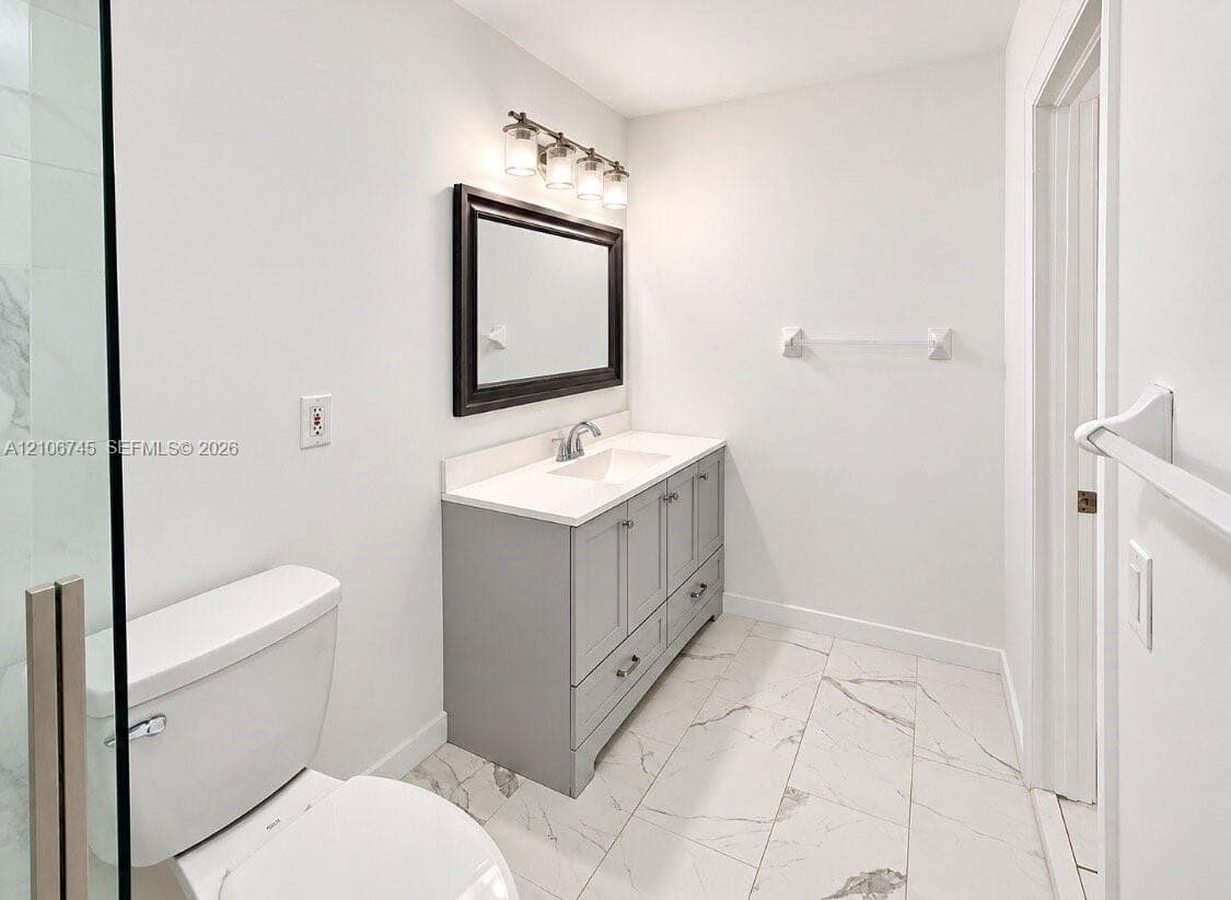 Bathroom featuring a gray vanity with an integrated countertop and basin, large-format tile flooring, a framed wall mirror, and a glass-enclosed shower