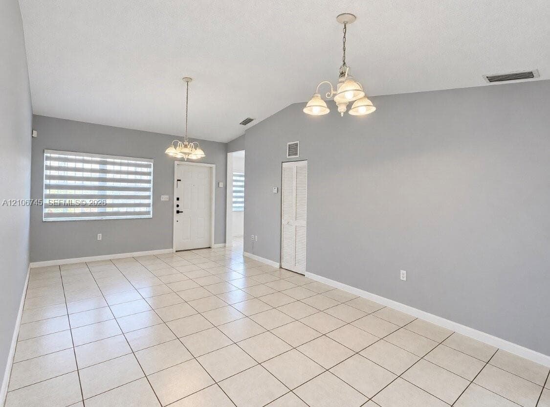 Open interior featuring high vaulted ceilings, large-format tile flooring, dual multi-arm chandeliers, and crisp neutral wall tones