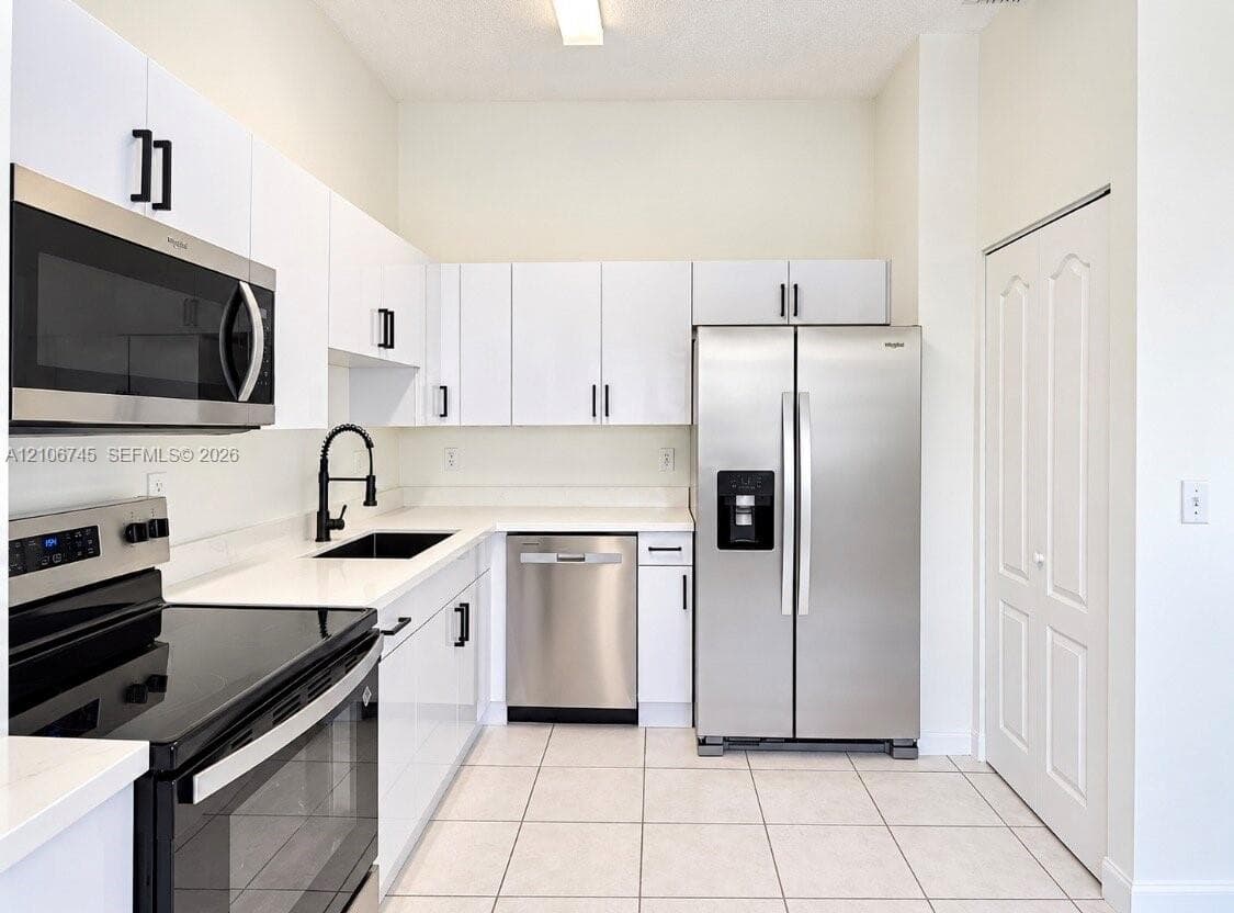 Kitchen featuring white cabinetry, quartz countertops, stainless steel appliances, a black faucet with undermount sink, and tiled flooring