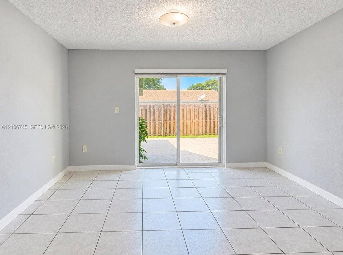 Neutral-toned interior featuring large-format ceramic tile flooring, sliding glass patio door, and flush-mount ceiling lighting