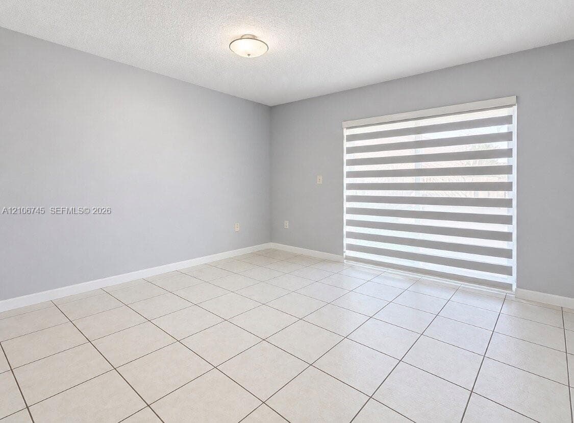 Neutral-toned interior featuring large-format ceramic tile flooring, sliding glass door with horizontal-banded roller shades, and flush-mount ceiling lighting