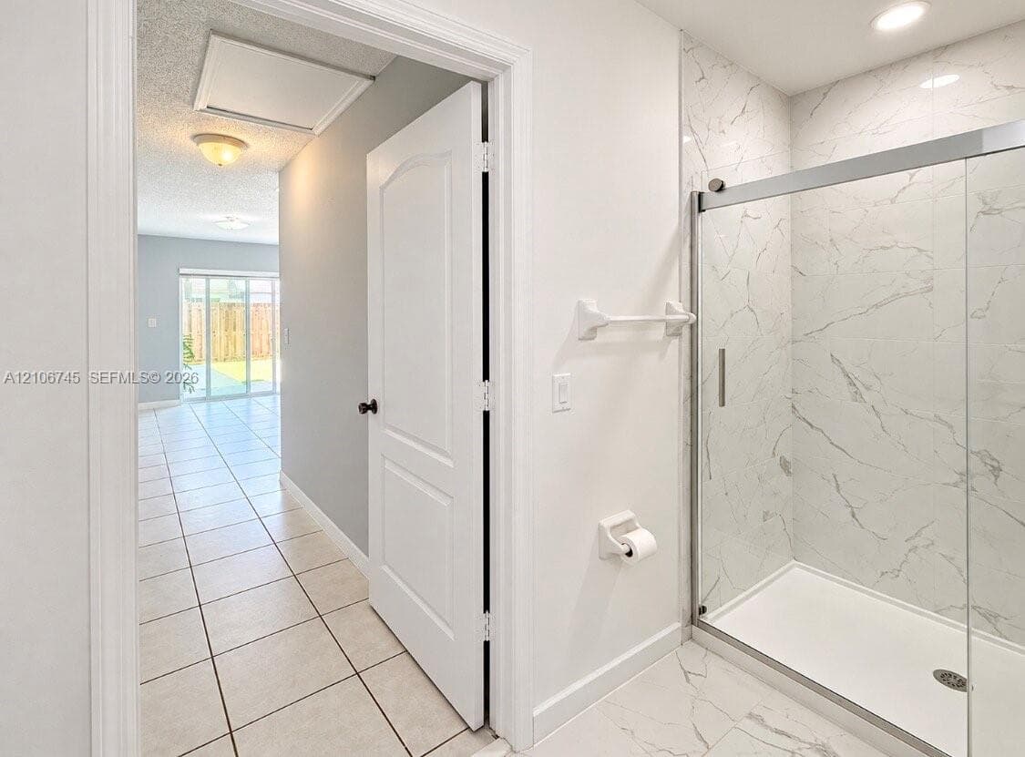 Bathroom featuring a walk-in shower with stone-patterned tile surround, glass sliding enclosure, and light-toned ceramic floor tiling