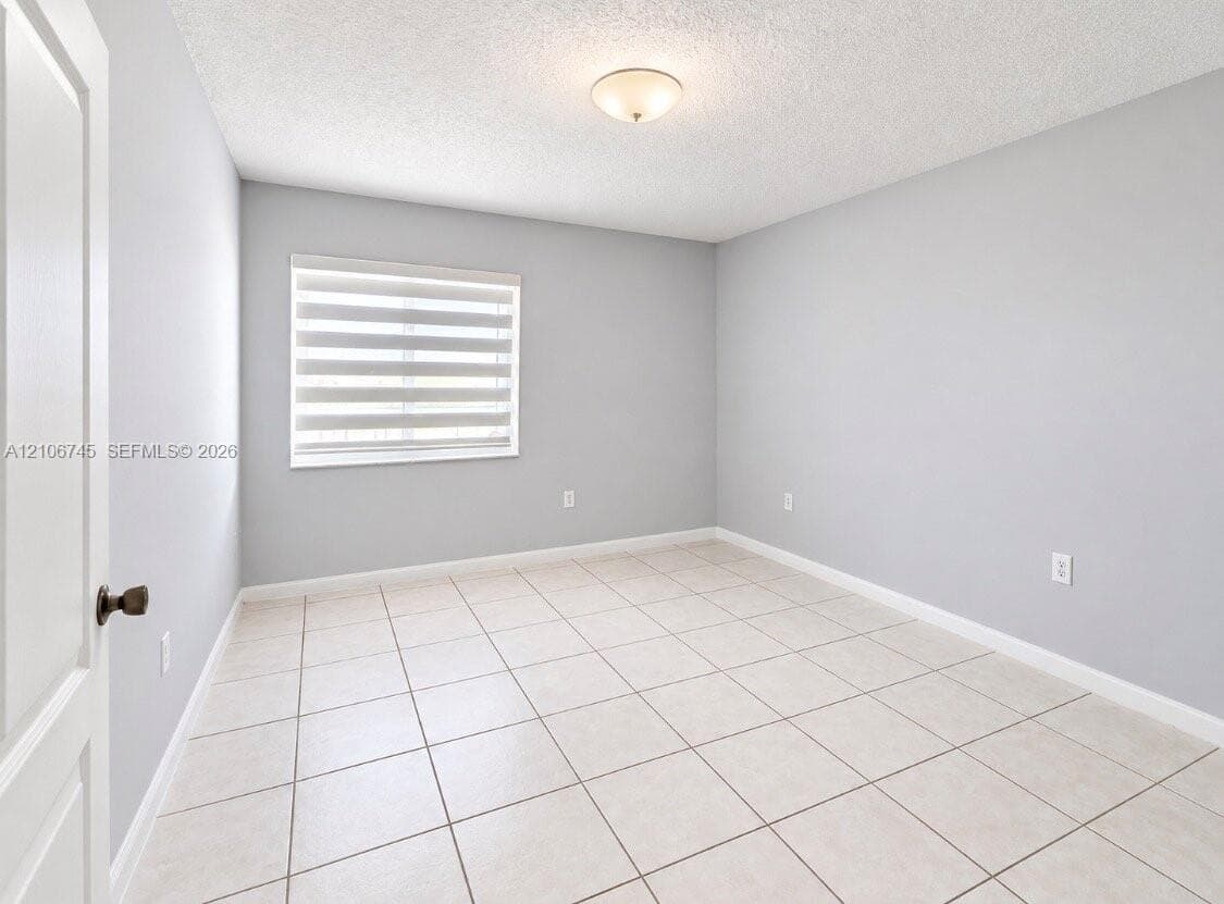 Neutral-toned interior space featuring tile flooring, a window with installed roller shades, and a ceiling-mounted dome light fixture