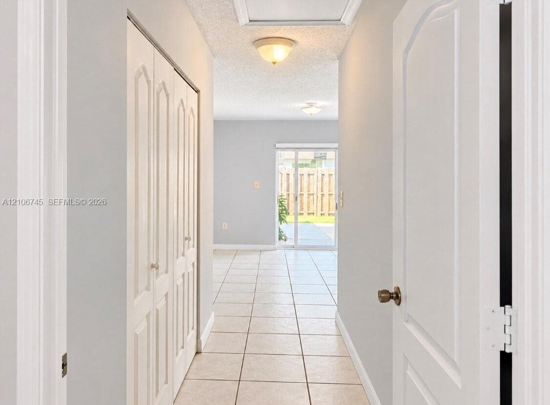 Hallway featuring neutral-toned tile flooring, bi-fold closet doors, and sliding glass exterior doors