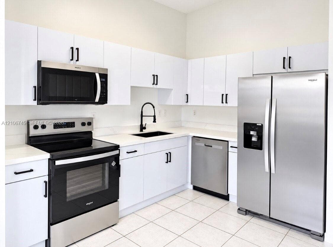 Kitchen featuring white flat-panel cabinetry, stainless steel appliances, solid surface countertops, a matte black high-arch faucet, and tile flooring