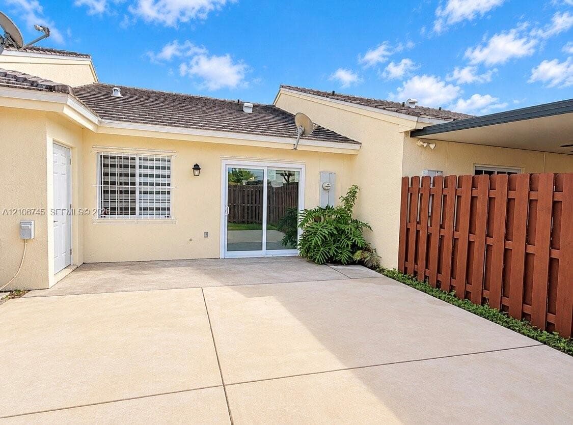 Concrete patio featuring a sliding glass door, exterior wall-mounted lighting, and a wood privacy fence