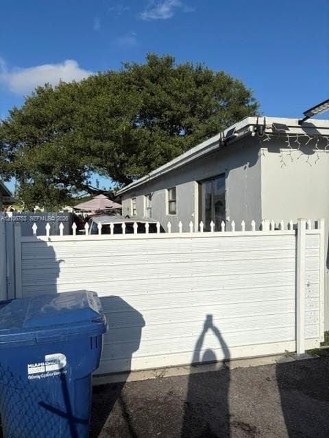 Exterior side profile featuring a white vinyl privacy fence with pointed picket accents and mature canopy tree