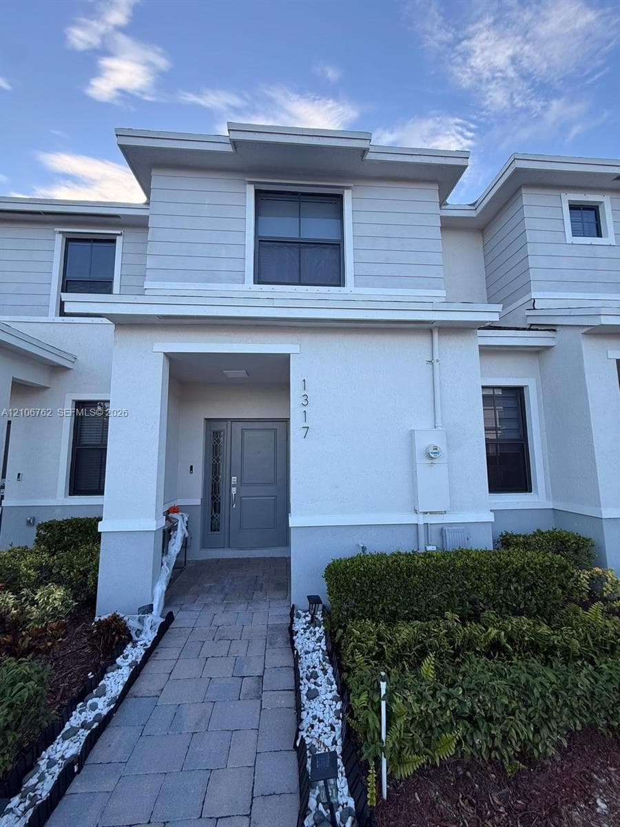 Exterior facade featuring a combination of horizontal lap siding and stucco finish, stone-paver walkway, and entrance door with decorative glass side panel
