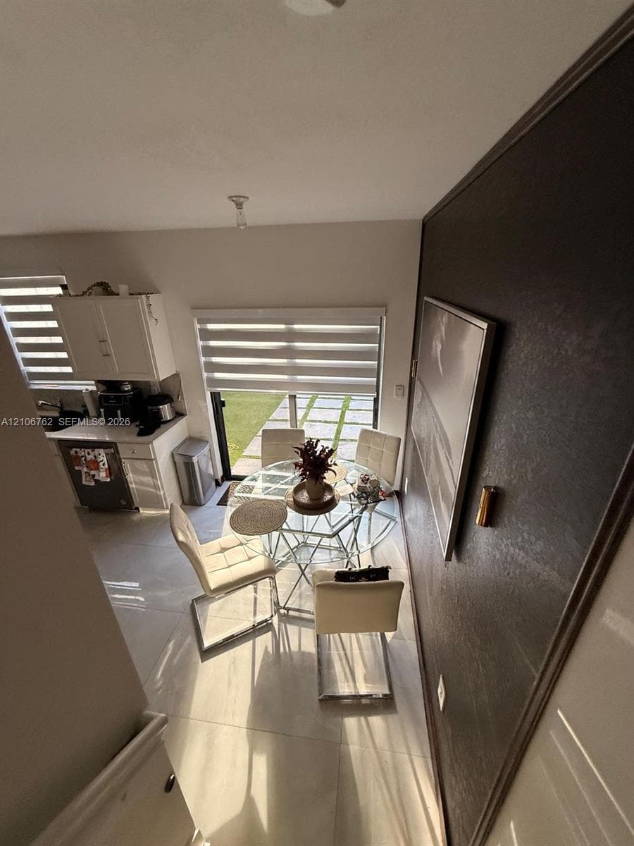 Large-format tile flooring, textured accent wall, sliding glass door, roller shade window treatments, and white cabinetry