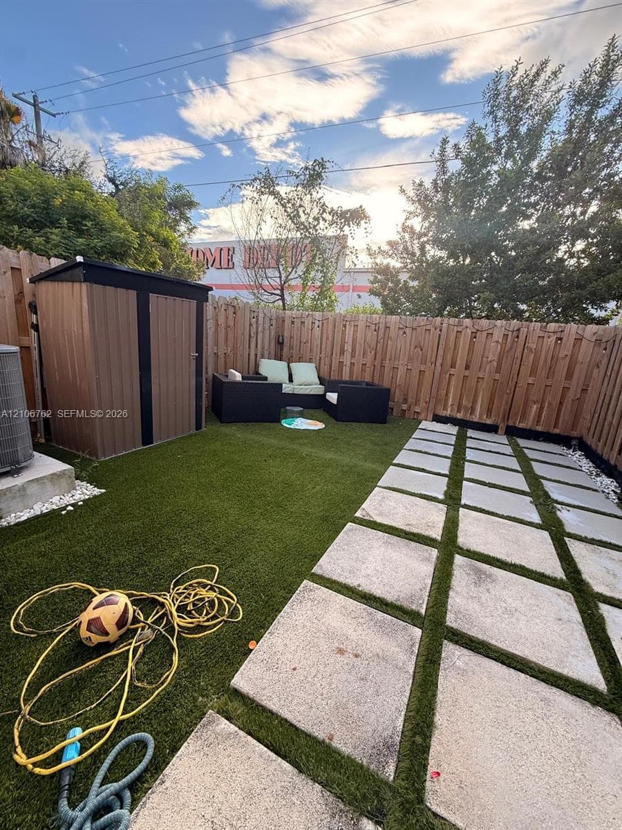 Backyard featuring synthetic turf, concrete paver hardscaping, a vertical wood privacy fence, and an integrated storage shed