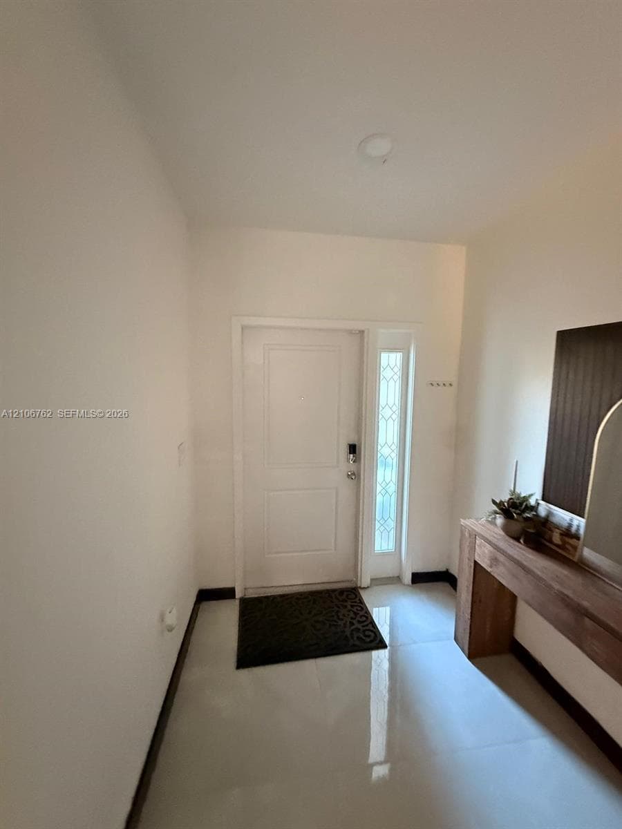 Entryway featuring a solid panel front door, tall glass sidelight with decorative metal grille, recessed ceiling lighting, and large-format tile flooring