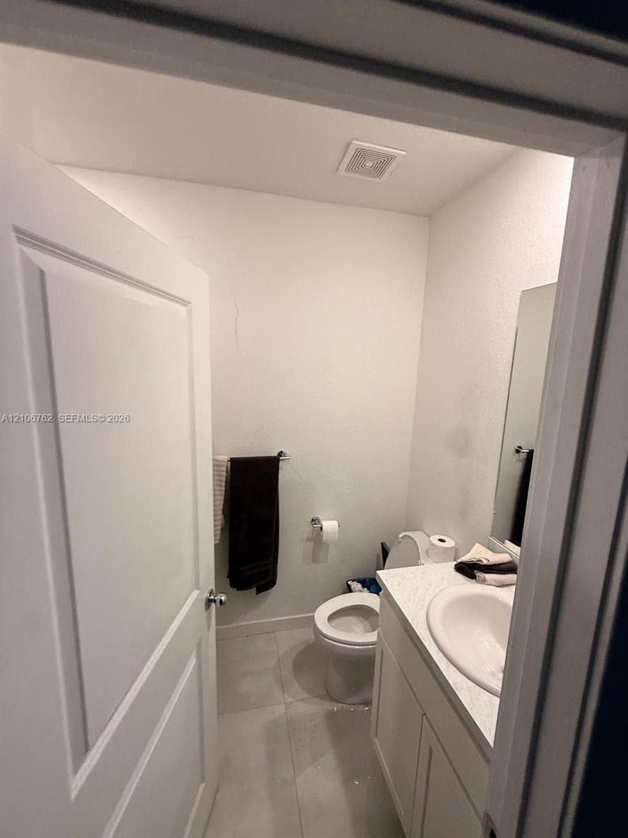 Restroom featuring a vanity with an integrated sink, stone-finish countertop, white cabinetry, a rectangular wall-mounted mirror, and ceramic tile flooring