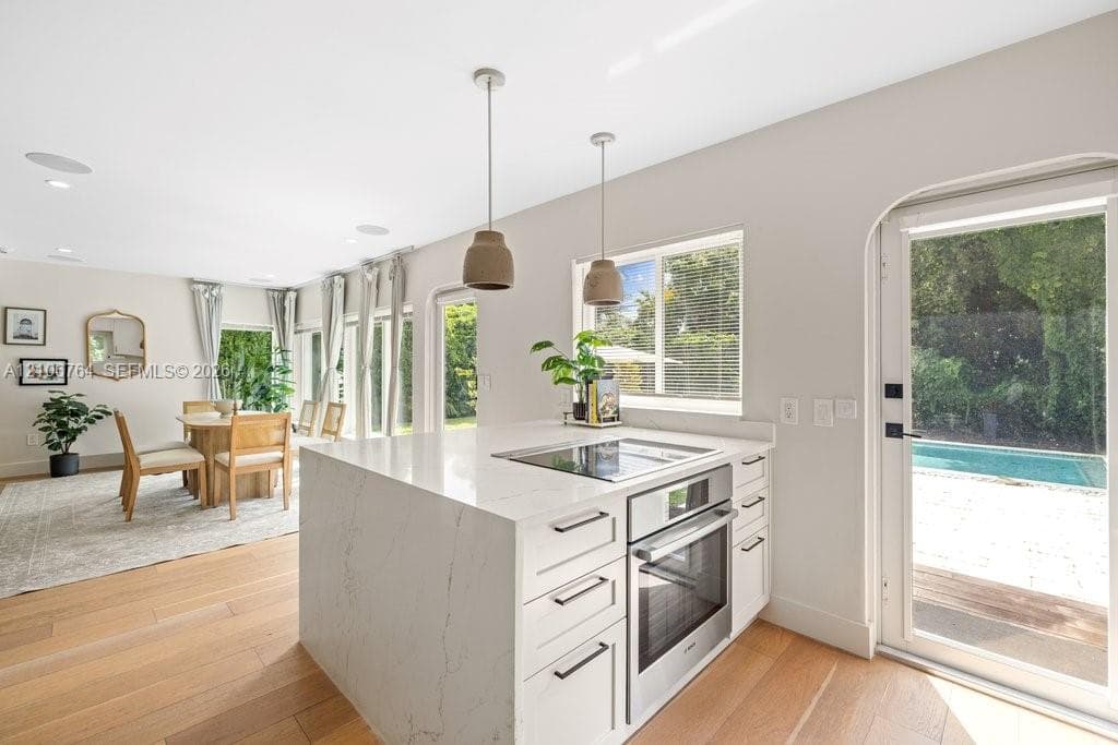 Kitchen island featuring a stone-look countertop, integrated cooktop, built-in oven, and white cabinetry, complemented by wood-finish flooring and pendant lighting