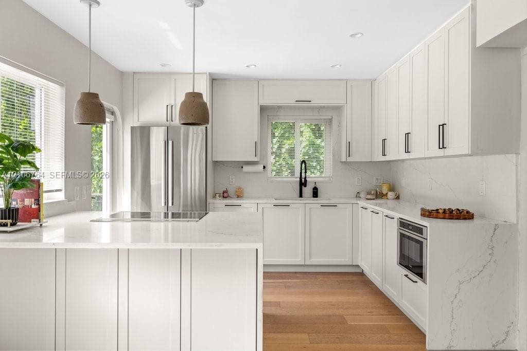 Kitchen featuring white cabinetry with matte black hardware, stone countertops with matching backsplash, wood-finish flooring, stainless steel built-in appliances, and dual pendant lighting