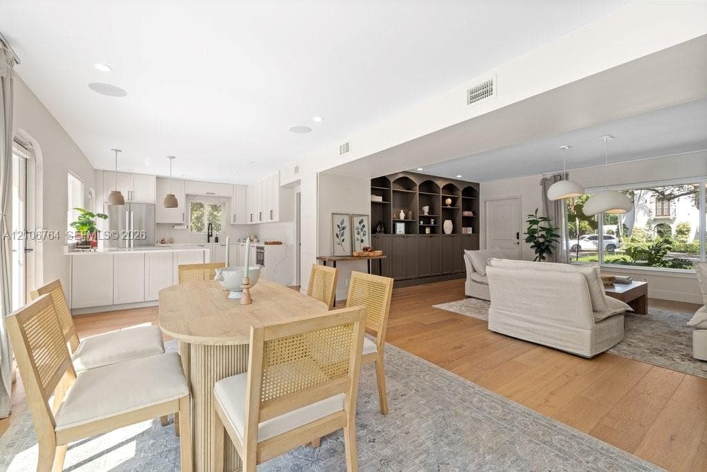 Open-concept kitchen and dining area featuring white shaker-style cabinetry, wood-finish flooring, custom built-in arched shelving, and recessed lighting