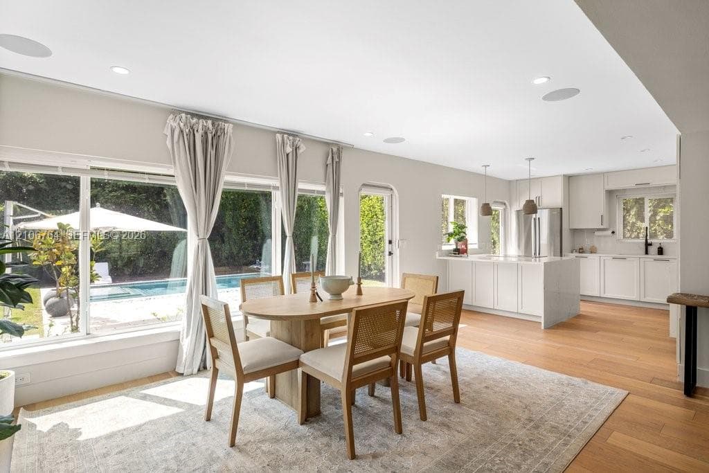 Open-concept kitchen and dining area featuring wood-finish flooring, recessed lighting, built-in ceiling speakers, and white cabinetry with a central kitchen island
