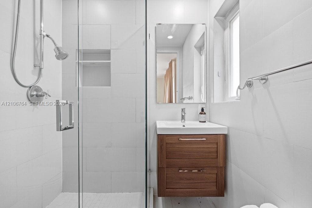 Bathroom featuring a wood-finish vanity with a rectangular sink, wall-mounted mirror, glass-enclosed shower with a built-in recessed niche, and polished metal fixtures