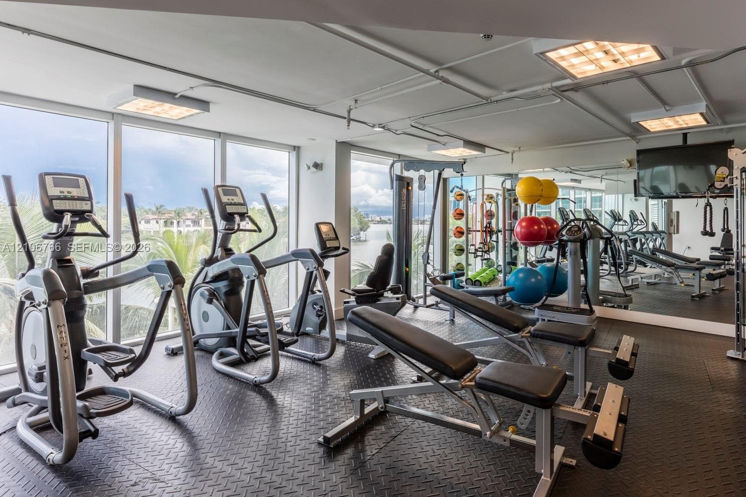 Fitness center featuring floor-to-ceiling windows, mirrored walls, textured rubber flooring, and exposed ceiling lighting