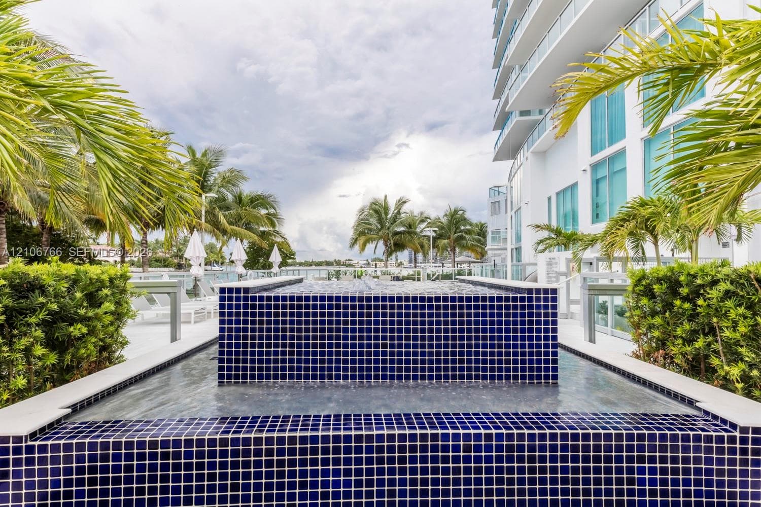 Outdoor water feature clad in cobalt blue tile, surrounded by manicured landscaping, palm trees, and structural glass balustrades