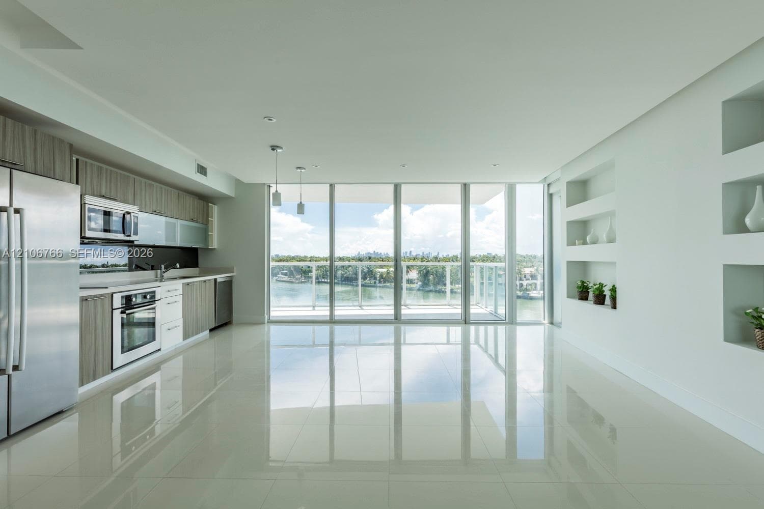 Contemporary kitchen featuring stainless steel appliances, wood-finish cabinetry, floor-to-ceiling glass paneling, polished tile flooring, and recessed wall shelving