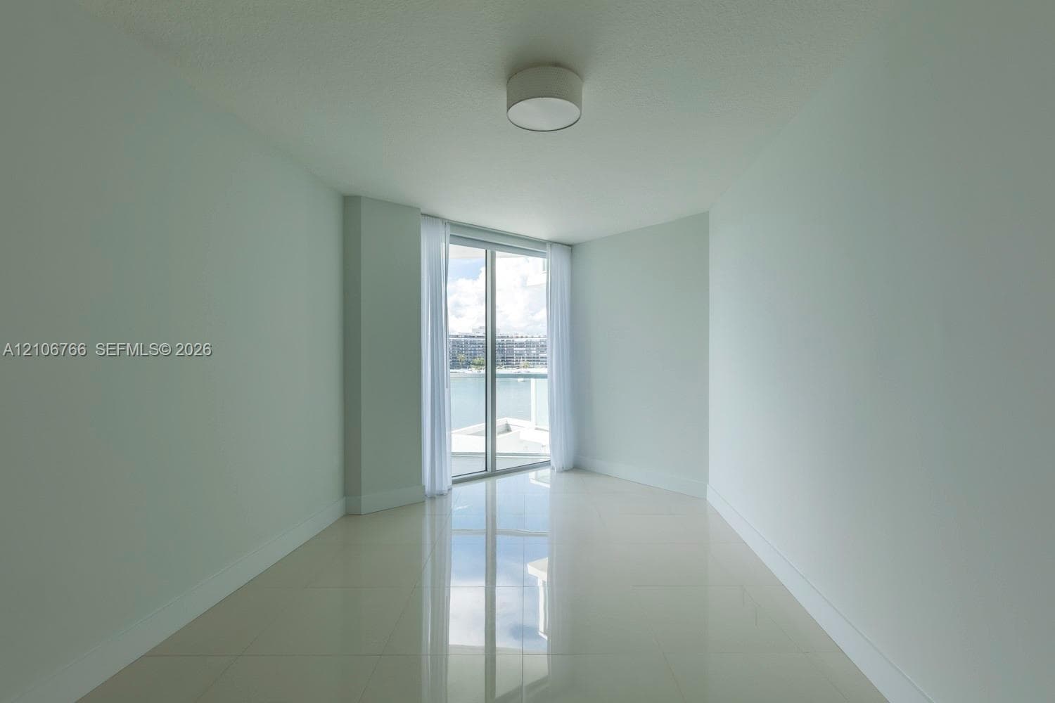 Neutral-toned interior space featuring polished tile flooring, a circular flush-mount ceiling light fixture, and full-height glass sliding doors