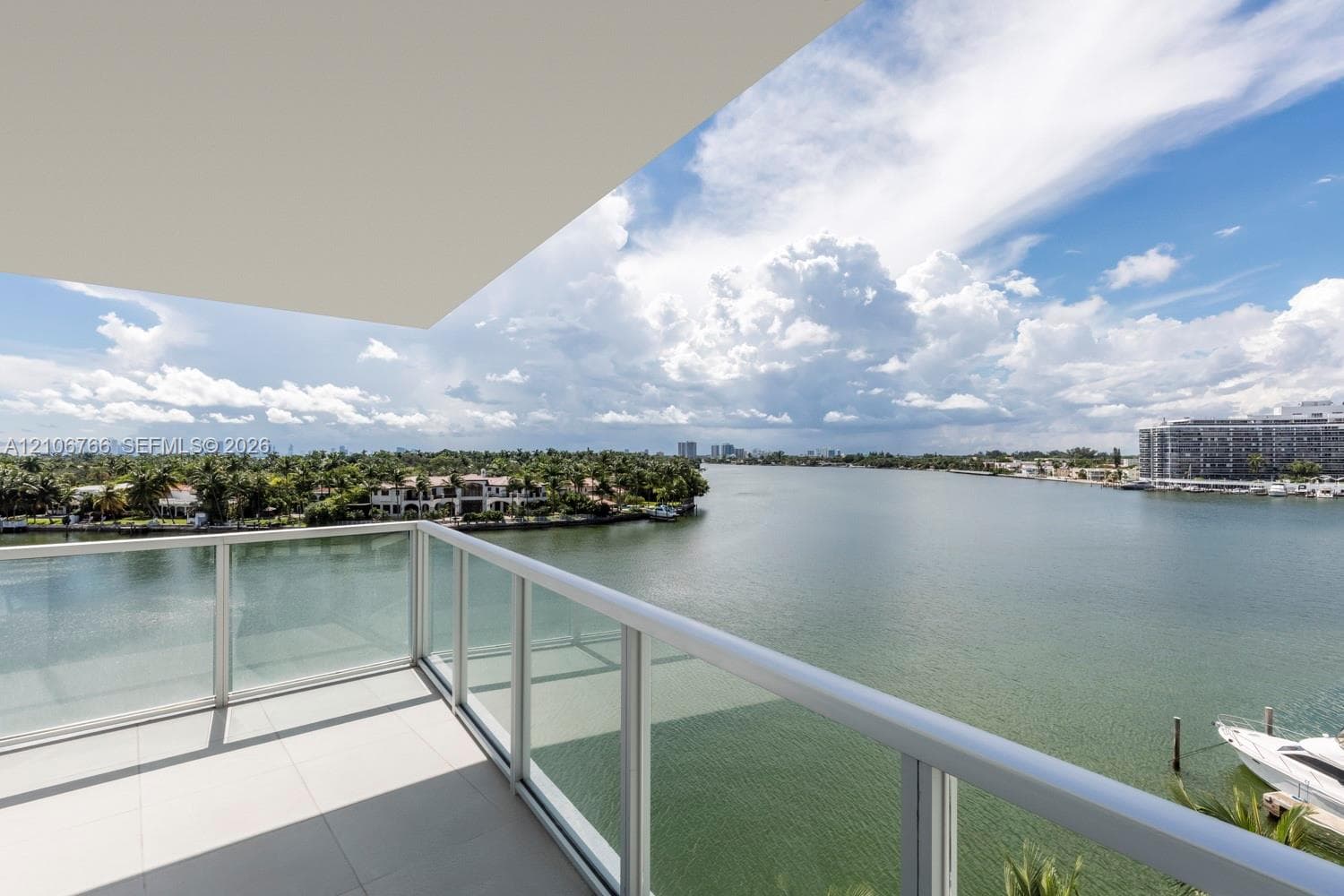 Private balcony featuring large-format tile flooring and a glass-paneled metal railing overlooking the waterfront