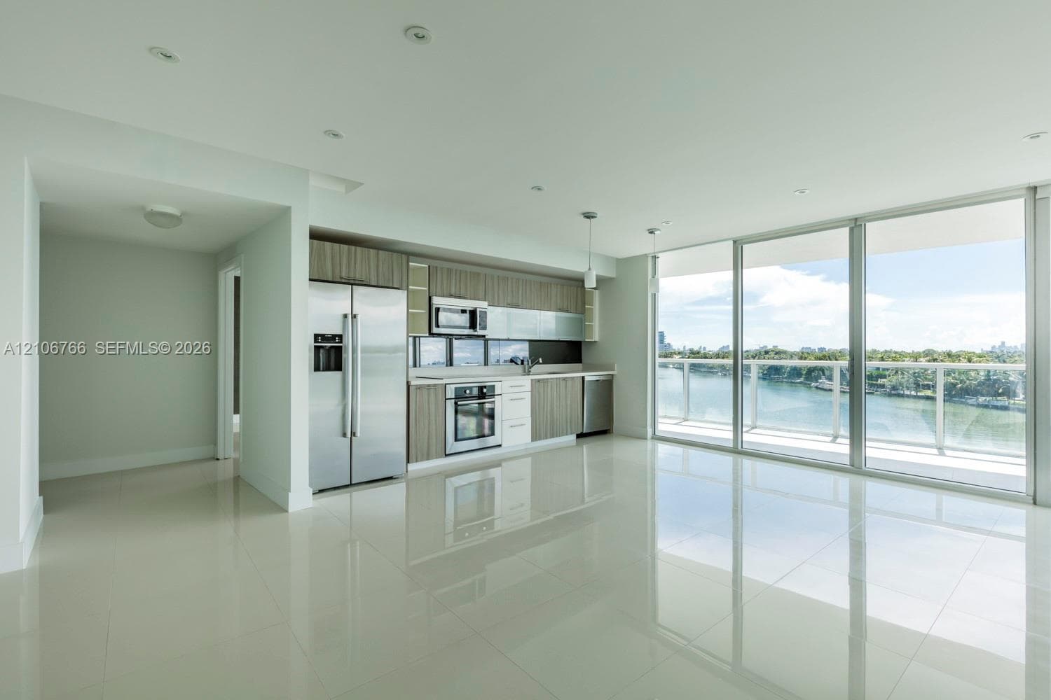 Open-concept interior featuring light-toned tile flooring, recessed ceiling lighting, stainless steel appliances, horizontally-grained cabinetry, and floor-to-ceiling glass panel doors